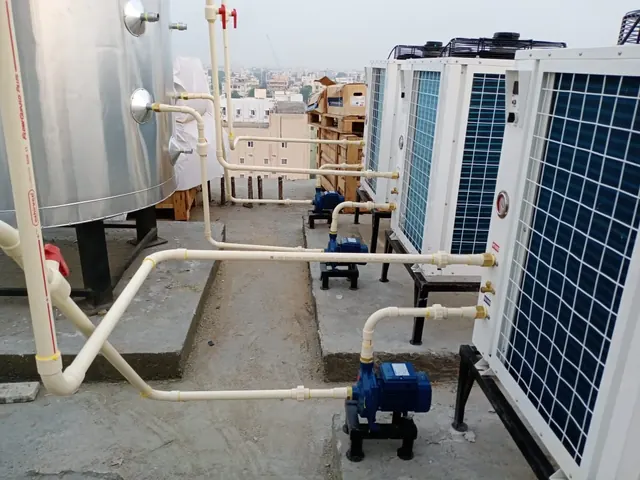 Bank of commercial heat pumps with circulation pumps and piping to a large stainless steel tank